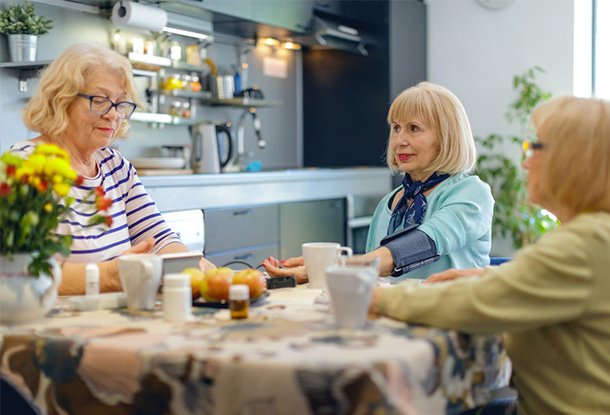 photo: three senior women at a table, one getting blood pressure taken (iStockphoto)