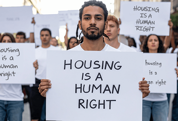 image: peaceful protesters holding signs reading "Housing is a human right" (Adobe Firefly)